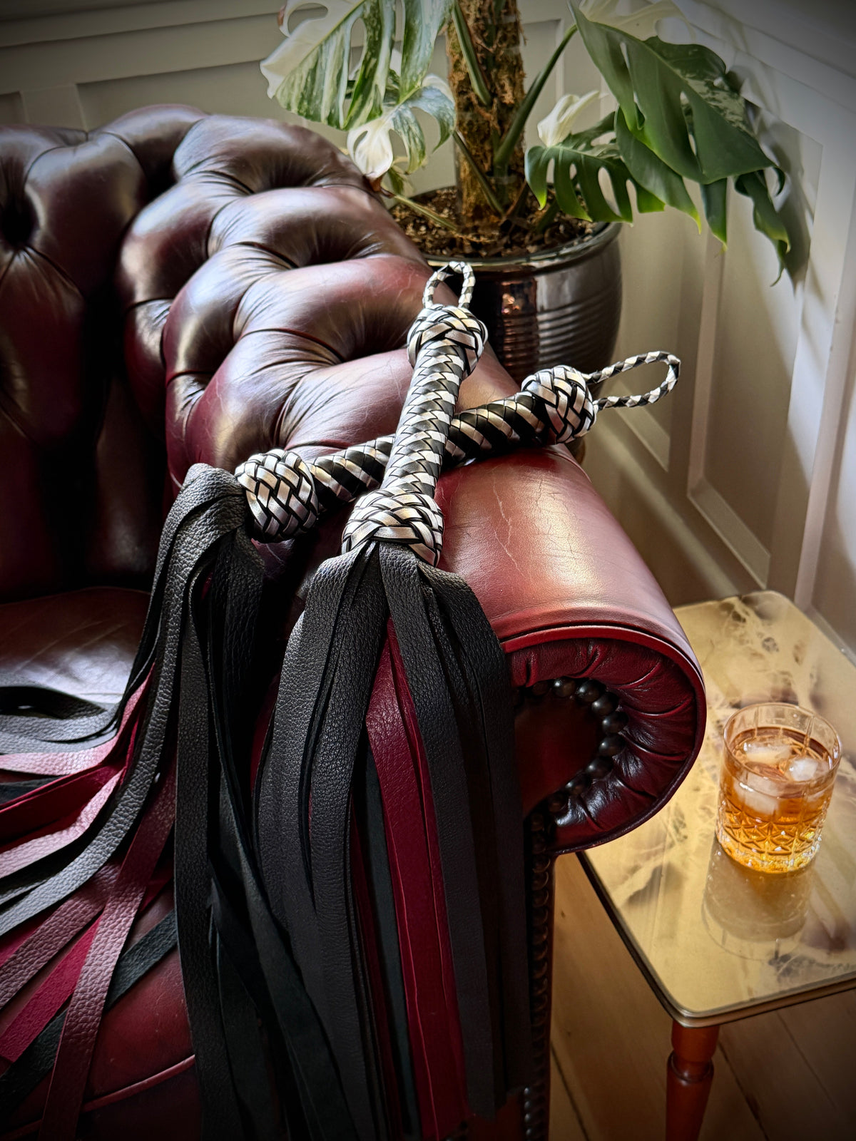 Black and red leather floggers on an oxblood Chesterfield beside a glass of whisky, The Whisky Room by Collared Foxy